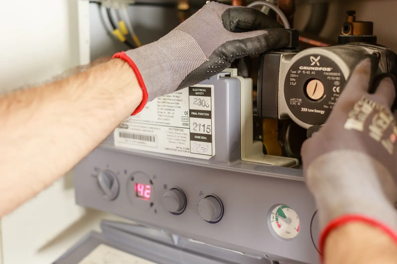 Mains d'un chauffagiste réglant les organes d'une chaudière murale, instrument de mesure à l'appui