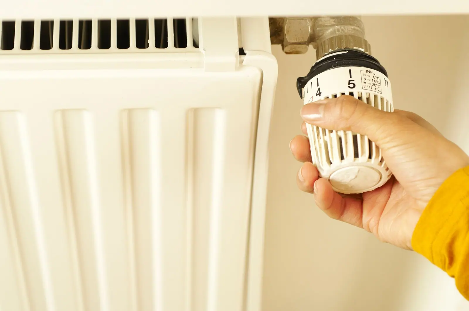 Main réglant le robinet thermostatique d'un radiateur pour ajuster le chauffage