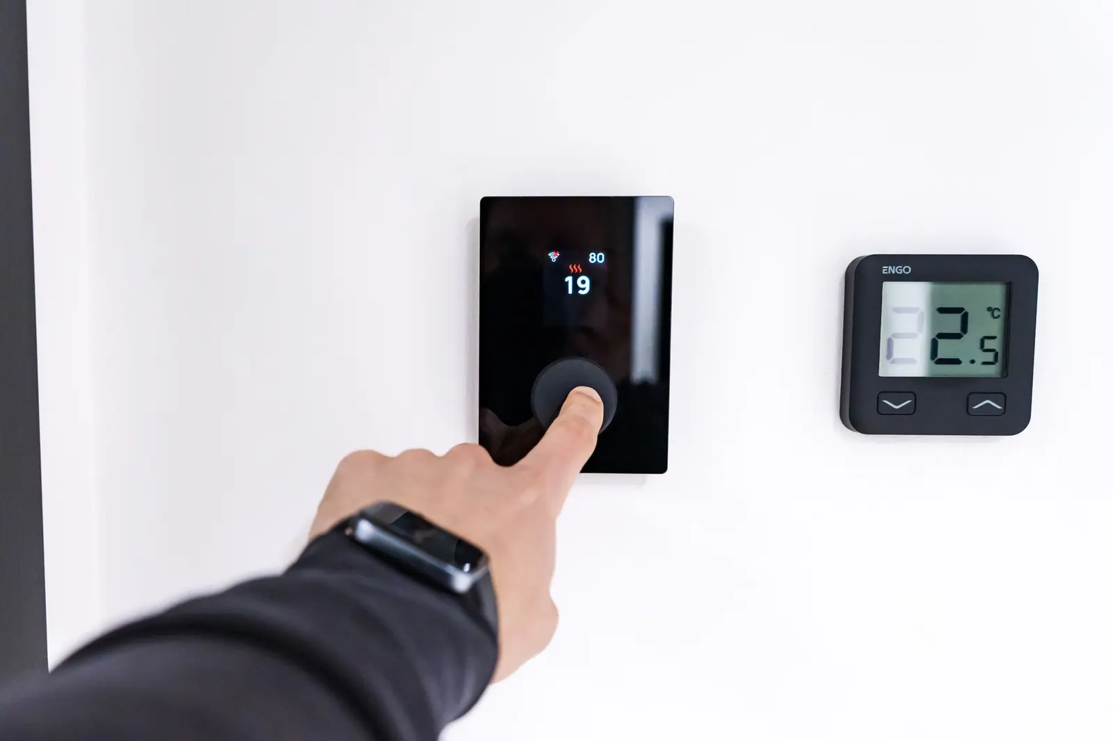 Main ajustant un thermostat connecté mural dans un intérieur contemporain